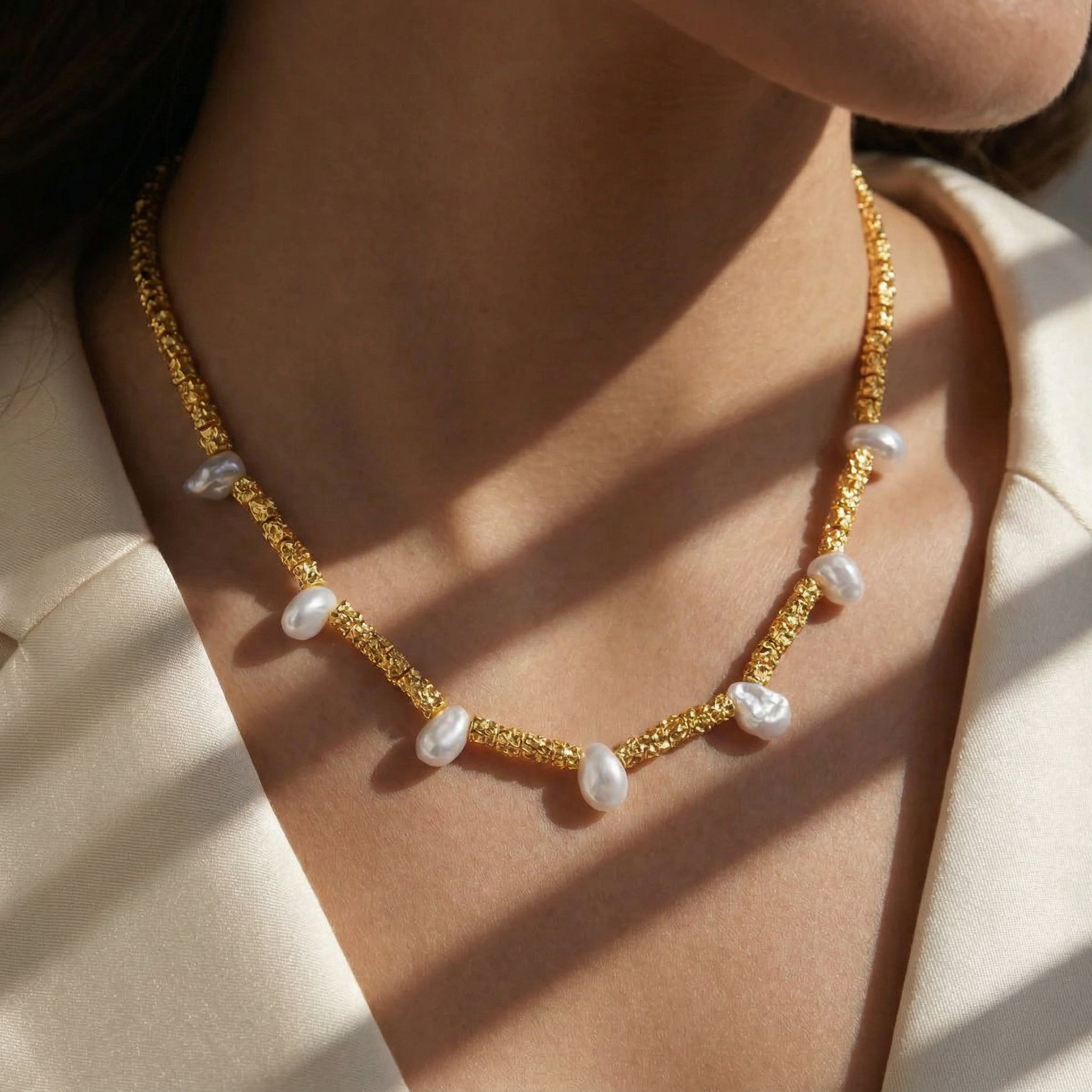Helena George. Gold necklace with pearls worn by a person against a neutral background